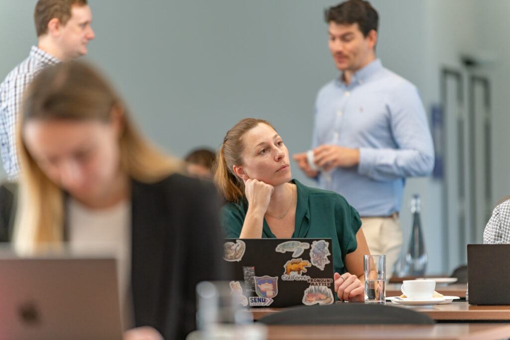 A woman sitting down at a table at her laptop listening to a presentation